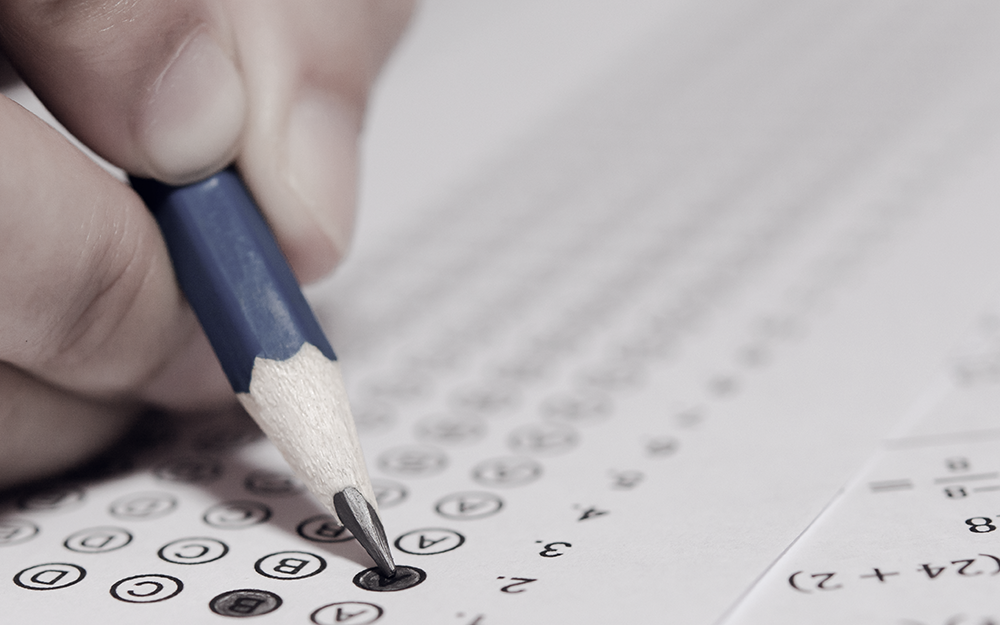 Part of a hand holding a pencil filling a bubble sheet.